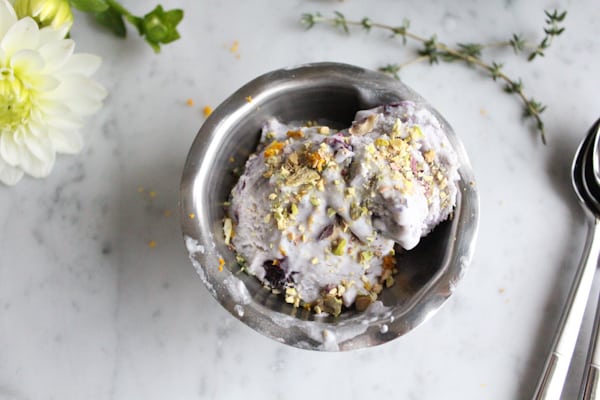 A dish of Blueberry Lemon and Thyme Ice Cream garnished with pistachio, lemon zest, and thyme.
