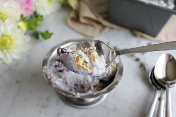 A spoonful of Blueberry Lemon and Thyme Ice Cream garnished with pistachio, lemon zest, and thyme.