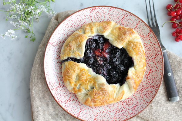 A mini berry galette on a plate with a napkin, berries, and flowers.