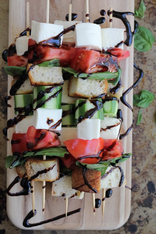 A stack of Caprese kabobs with balsamic glaze on a wood cutting board.