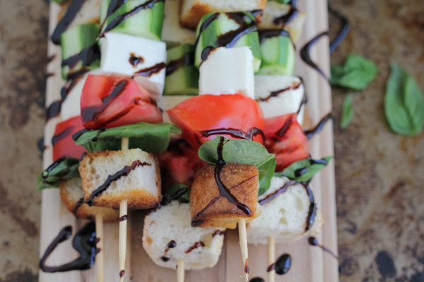 Caprese kabobs with balsamic glaze on a wood cutting board.
