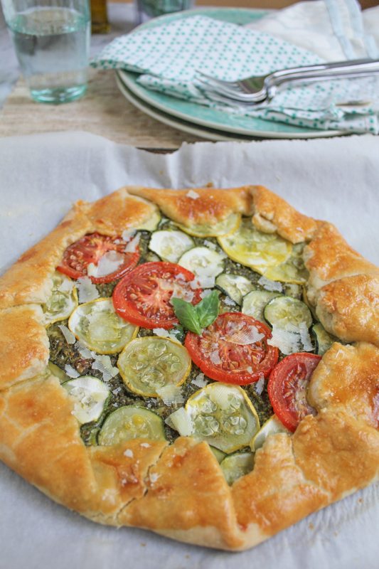 Summer Vegetable Galette with Pesto on a piece of parchment paper with plates, napkins, and silverware in the background.