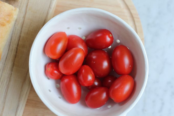 A small white bowl with tomatoes on a wood surface.