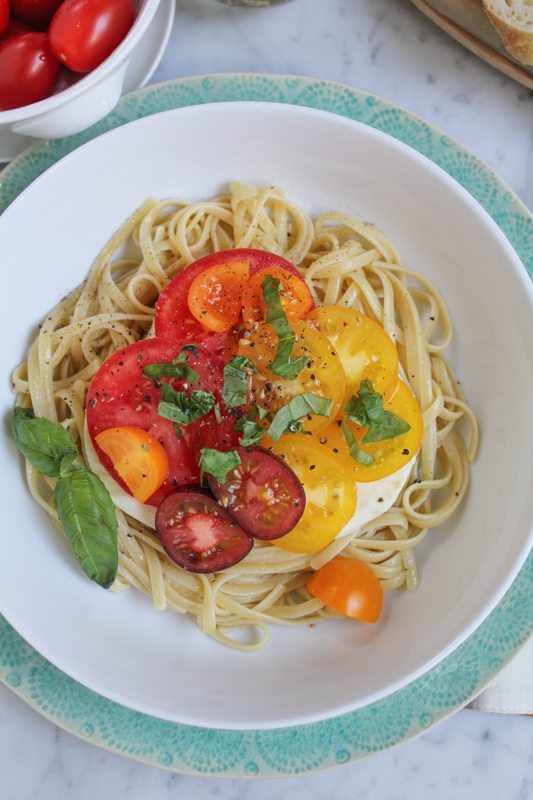 A bowl of Summer Caprese pasta salad with a small white bowl of tomatoes.