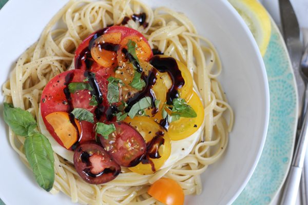 A bowl of Summer Caprese pasta salad drizzled with balsamic vinegar.