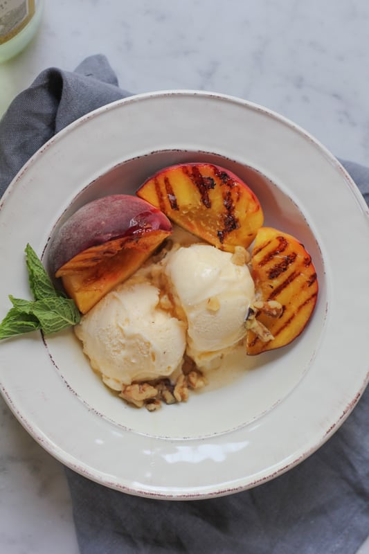 Vanilla Ice Cream with Grilled Peaches in a white bowl, with a gray napkin.