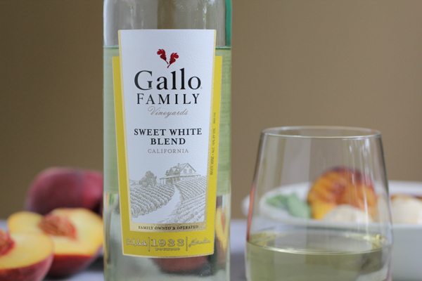 A bottle of white wine, a glass of white wine, and peaches.