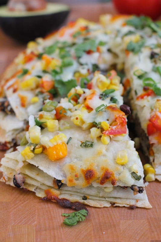 Close up photo of a sliced Corn and Black Bean Tortilla Tart on a wood cutting board.