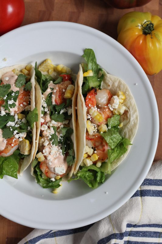 Grilled Shrimp Tacos with Mexican Crema on a white plate with a napkin and tomatoes.