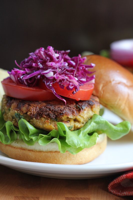 A chickpea burger topped with tomatoes and red cabbage slaw on a plate.