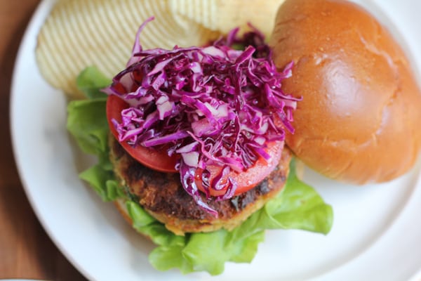 A chickpea burger topped with tomatoes and red cabbage slaw on a plate.