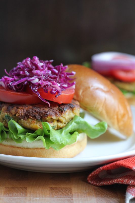 A chickpea burger topped with red cabbage slaw and tomatoes on a plate.