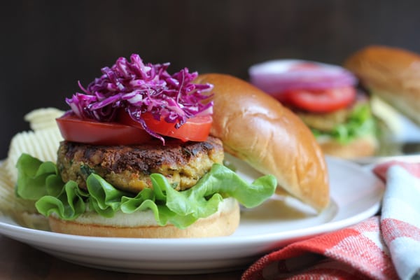A chickpea burger topped with tomatoes and red cabbage slaw on a plate.