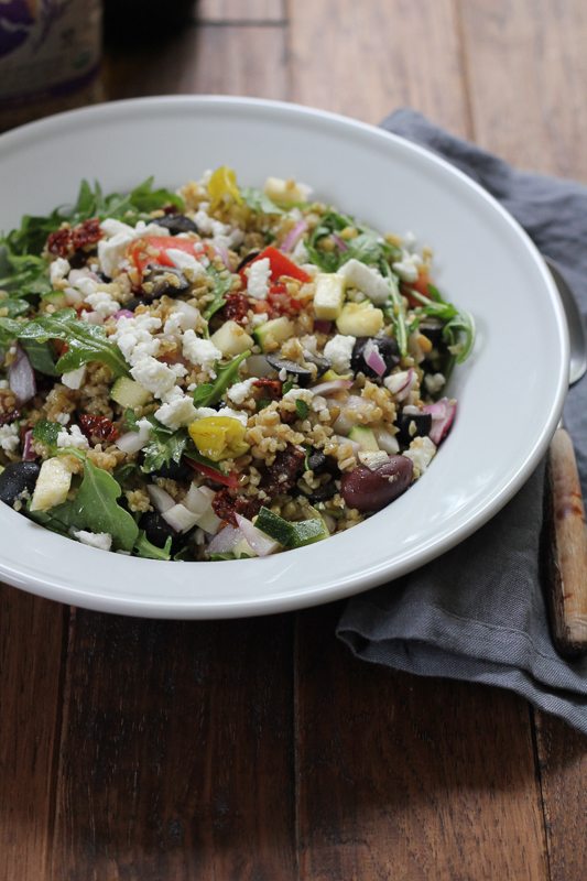 A bowl of Mediterranean Freekeh Salad in a white bowl on a wood surface.