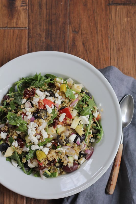 A bowl of Mediterranean Freekeh Salad on a wood surface.