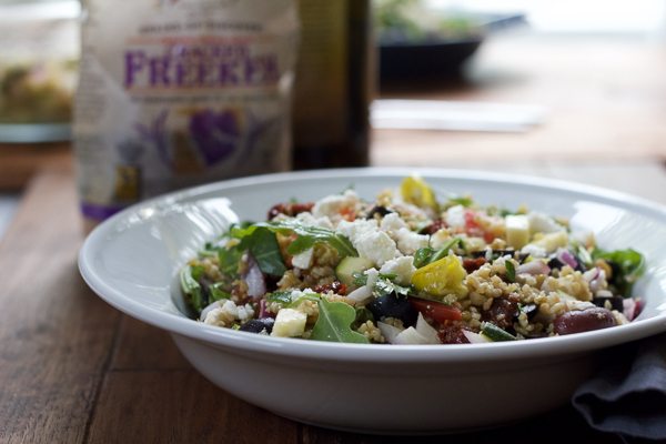 A bowl of Mediterranean Freekeh Salad with a bag of freekeh grains in the background.
