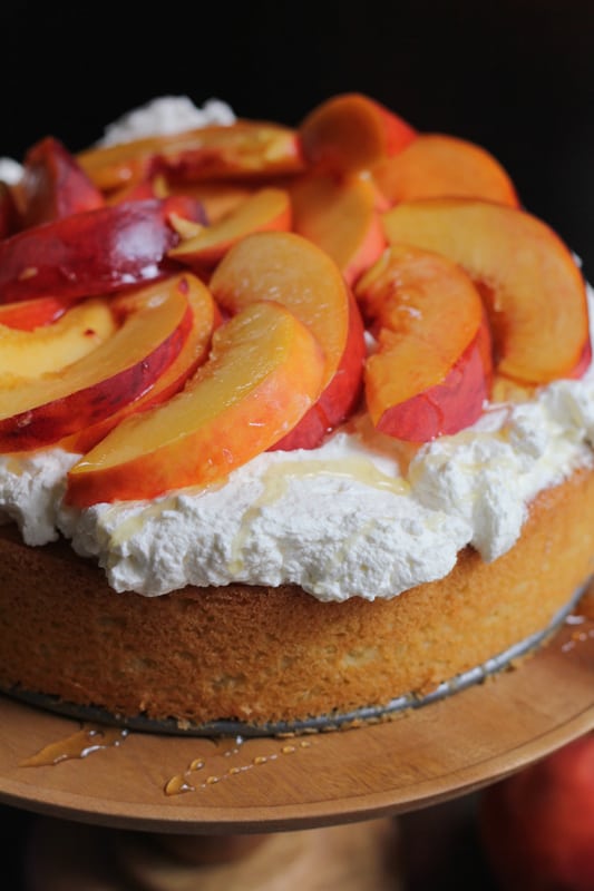 Olive Oil Honey Cake With Fresh Peaches on a wooden cake stand.