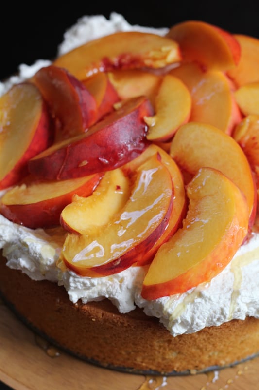 Close up photo of Olive Oil Honey Cake With Fresh Peaches on a wooden cake stand.