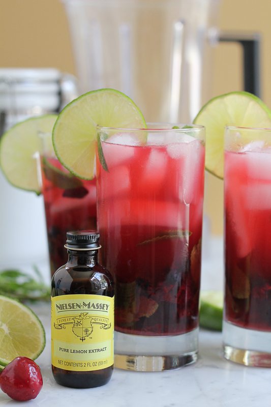 A bottle of lemon extract with glasses of blueberry cherry mojitos.