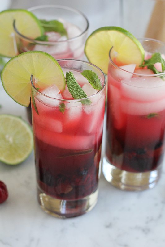 Three glasses of Blueberry Cherry Mojitos garnished with lime and mint.
