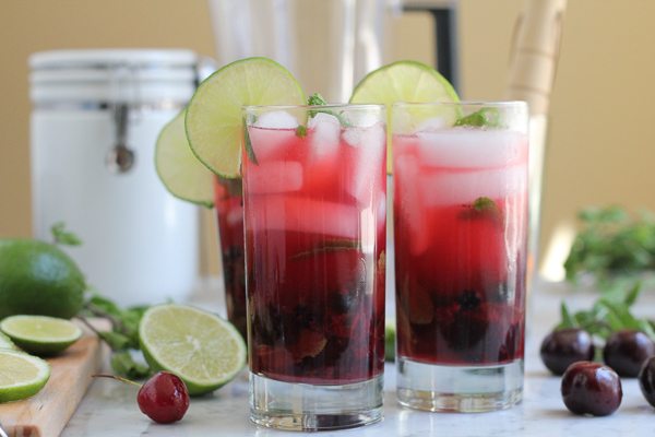 Glasses of Blueberry Cherry Mojitos with limes, cherries, and mint.