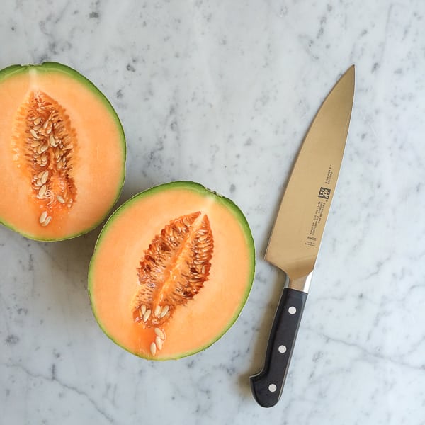A cantaloupe sliced in half for Simple Cantaloupe Salad and a knife.