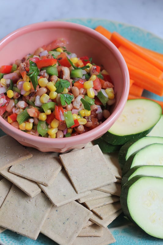 A bowl of Texas Caviar with sliced raw vegetables and crackers.