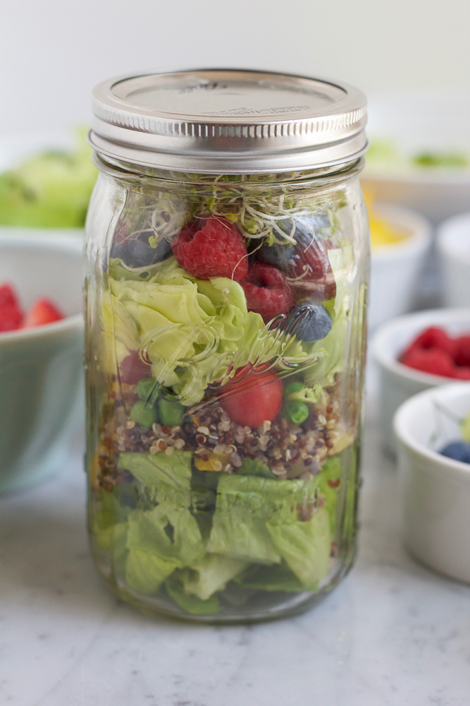 A jar of Mason Jar Salad with bowls of ingredients in the background.