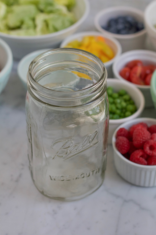 An empty mason jar for Mason Jar Salad with ingredients in bowls in the background.