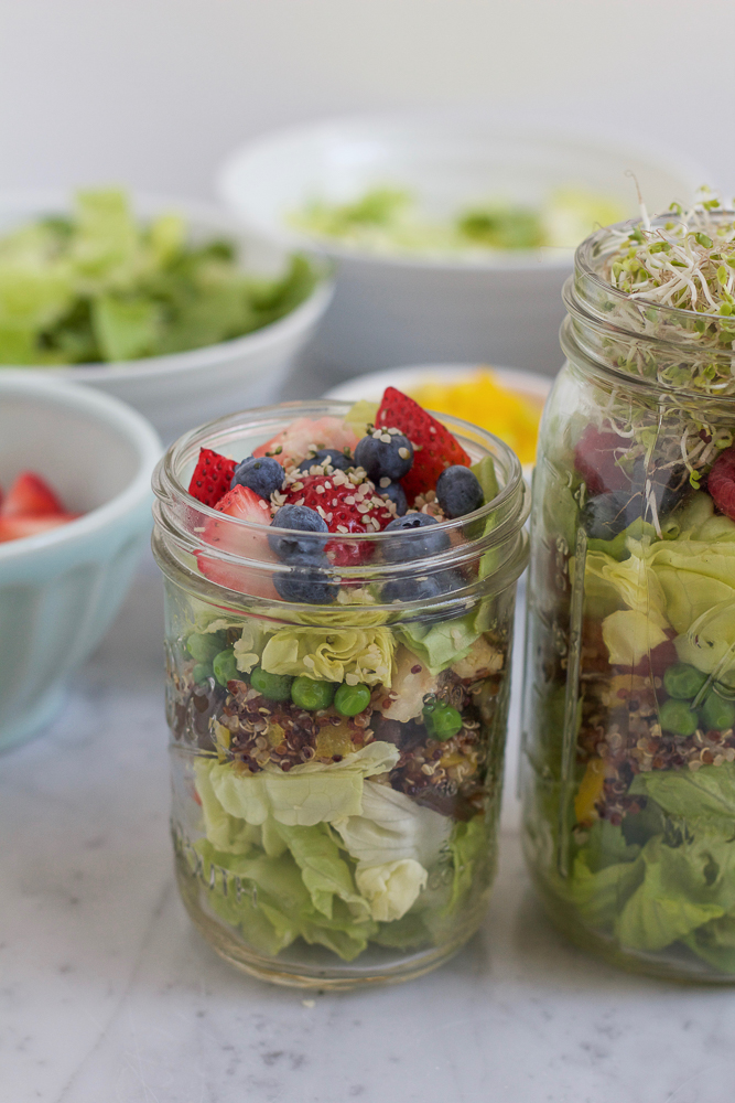 A small jar of Mason Jar Salad with ingredients in bowls in the background.