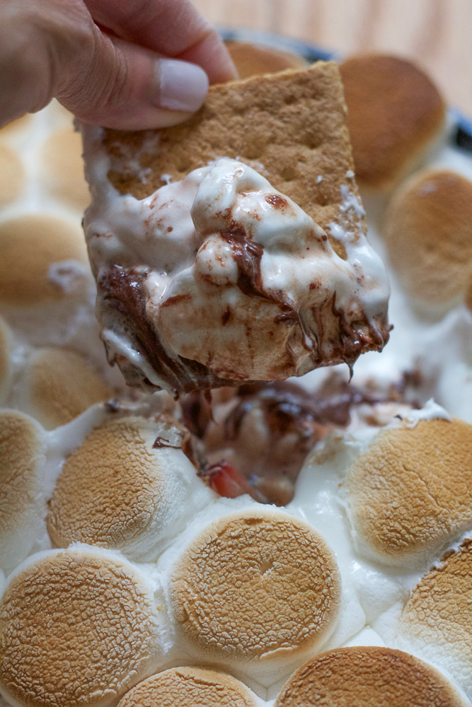 A graham cracker being dipped into a skillet of Easy S'mores Dip.