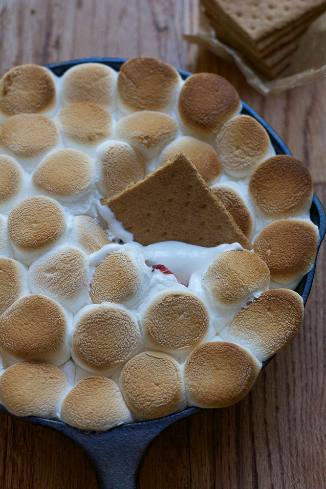 A skillet of Easy S'mores Dip with a graham cracker dipped in.
