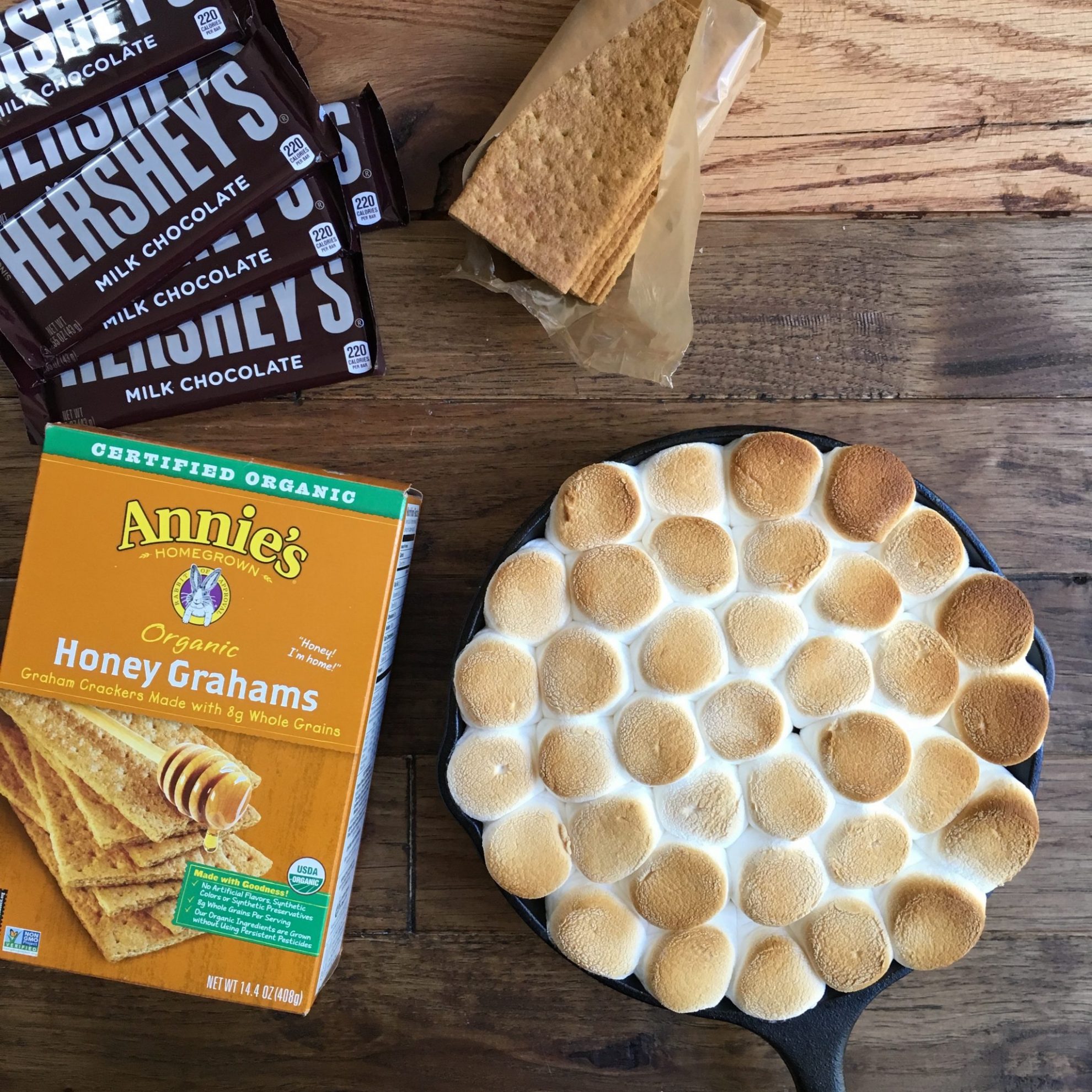 A skillet of easy s'mores dip next to a box of graham crackers, chocolate bars, and an open sleeve of graham crackers.