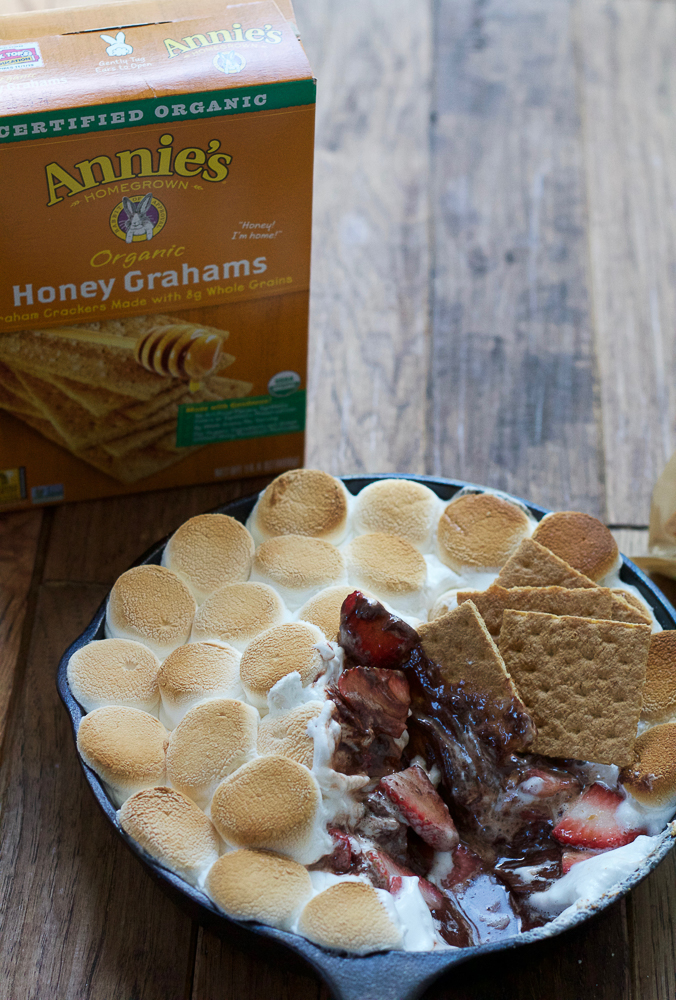 A skillet of Easy S'mores Dip with graham crackers dipped in it, with a box of graham crackers.