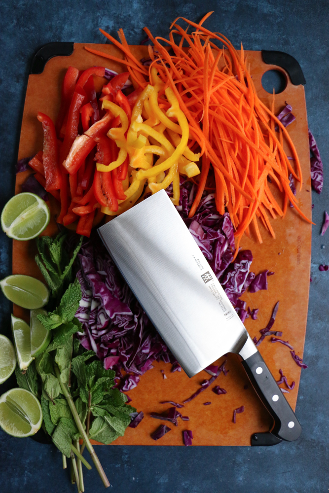 A board of chopped veggies for Chicken and Veggie Spring Rolls with a knife.