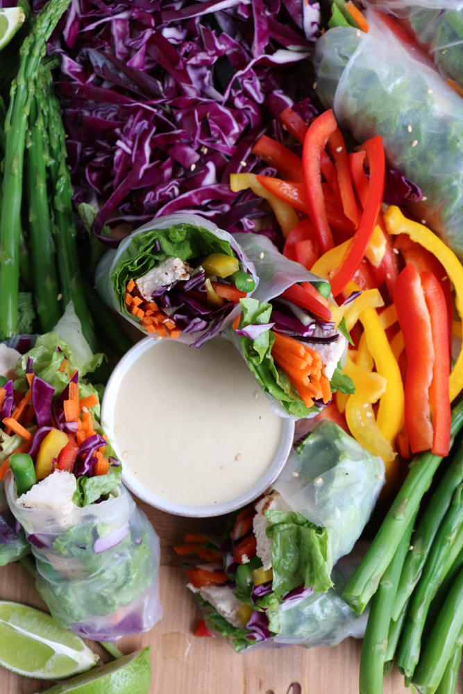Chopped vegetables, Chicken and Veggie Spring Rolls and a bowl of dipping sauce on a board.