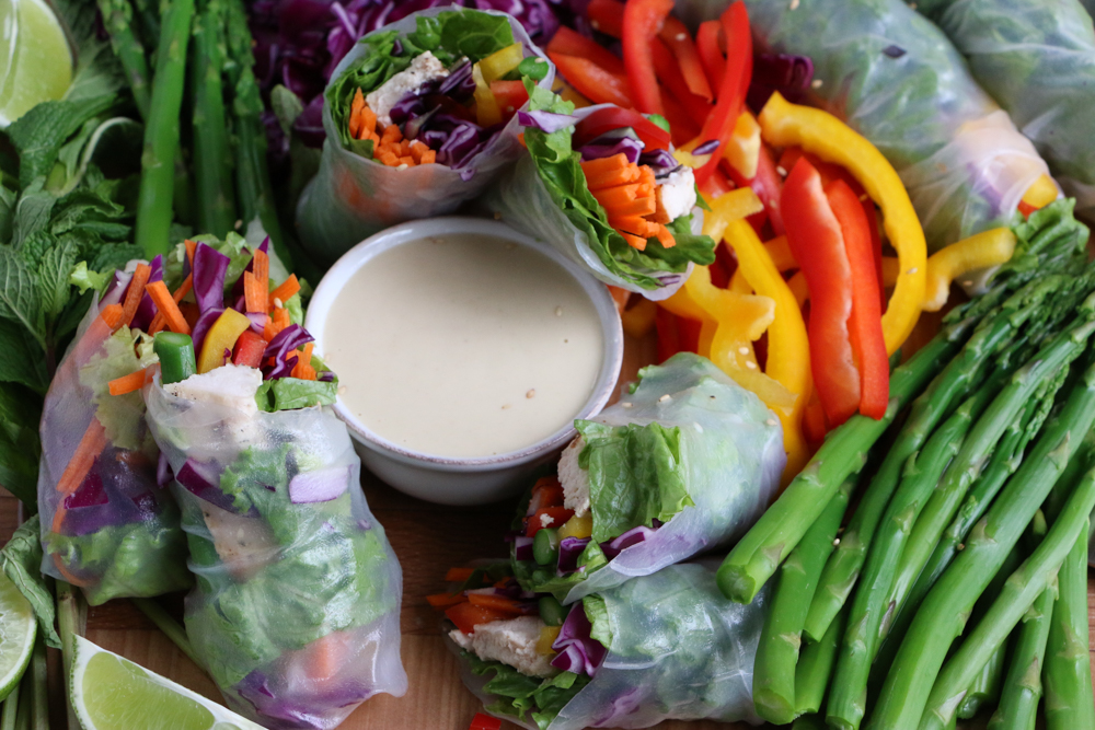 Chicken and Veggie Spring Rolls and chopped vegetables on a board with a bowl of dipping sauce.