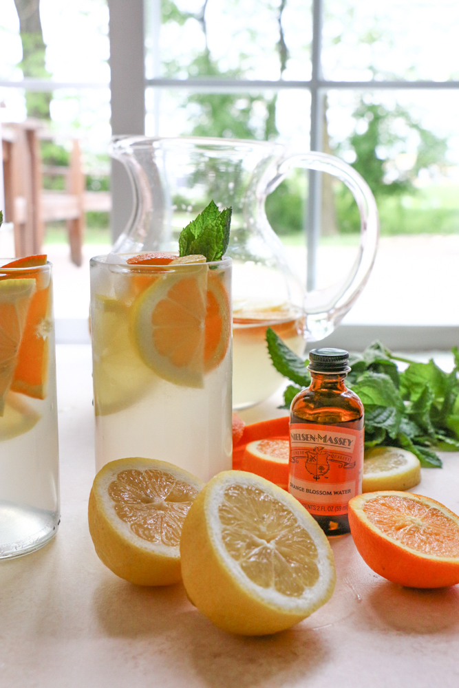 Glasses of Orange Blossom Lemonade with lemons, oranges, mint, and orange blossom water.