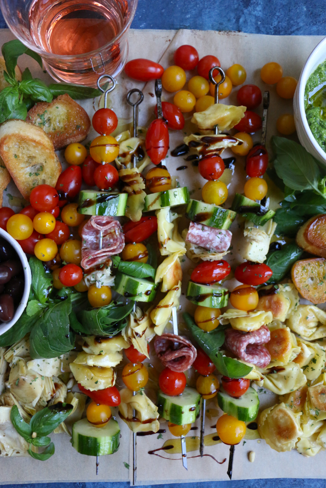 Summer Tortellini Pasta Salad on skewers surrounded by slices of bread and a glass of wine.