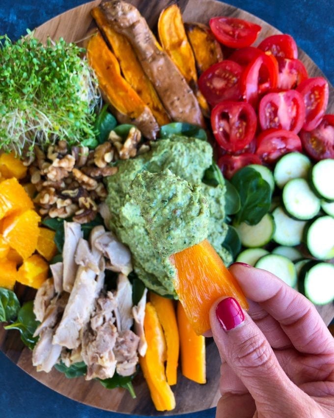 Bell pepper being dipped into Green Goddess Avocado Sauce on a veggie and fruit platter.