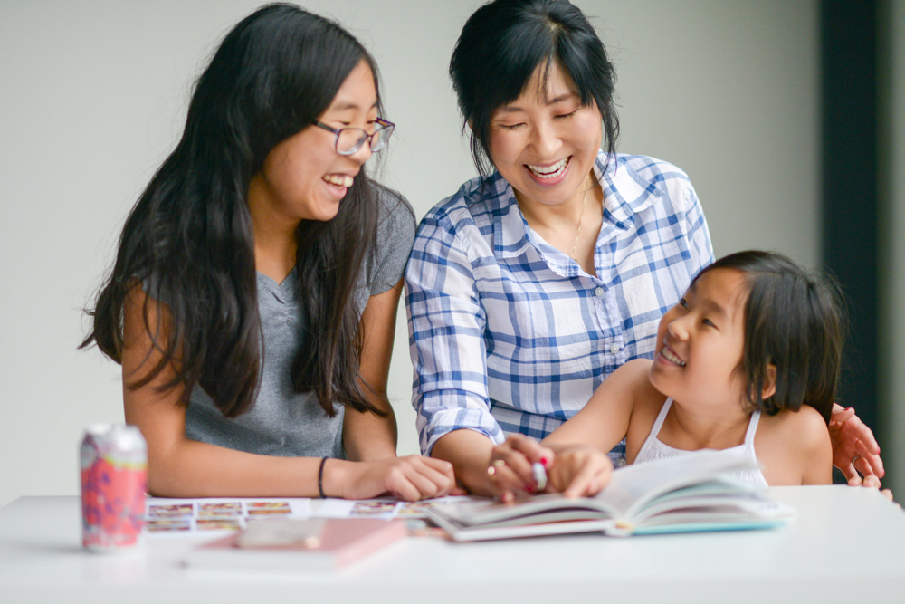 Asian mother and her 2 daughters looking at cookbook together
